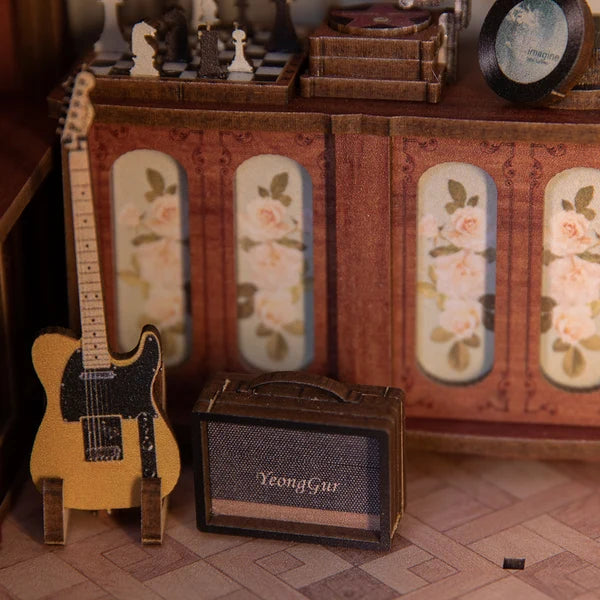 Miniature elguitar og lille forstærker med teksten 'YeongGur' foran blomsterdekoreret skab